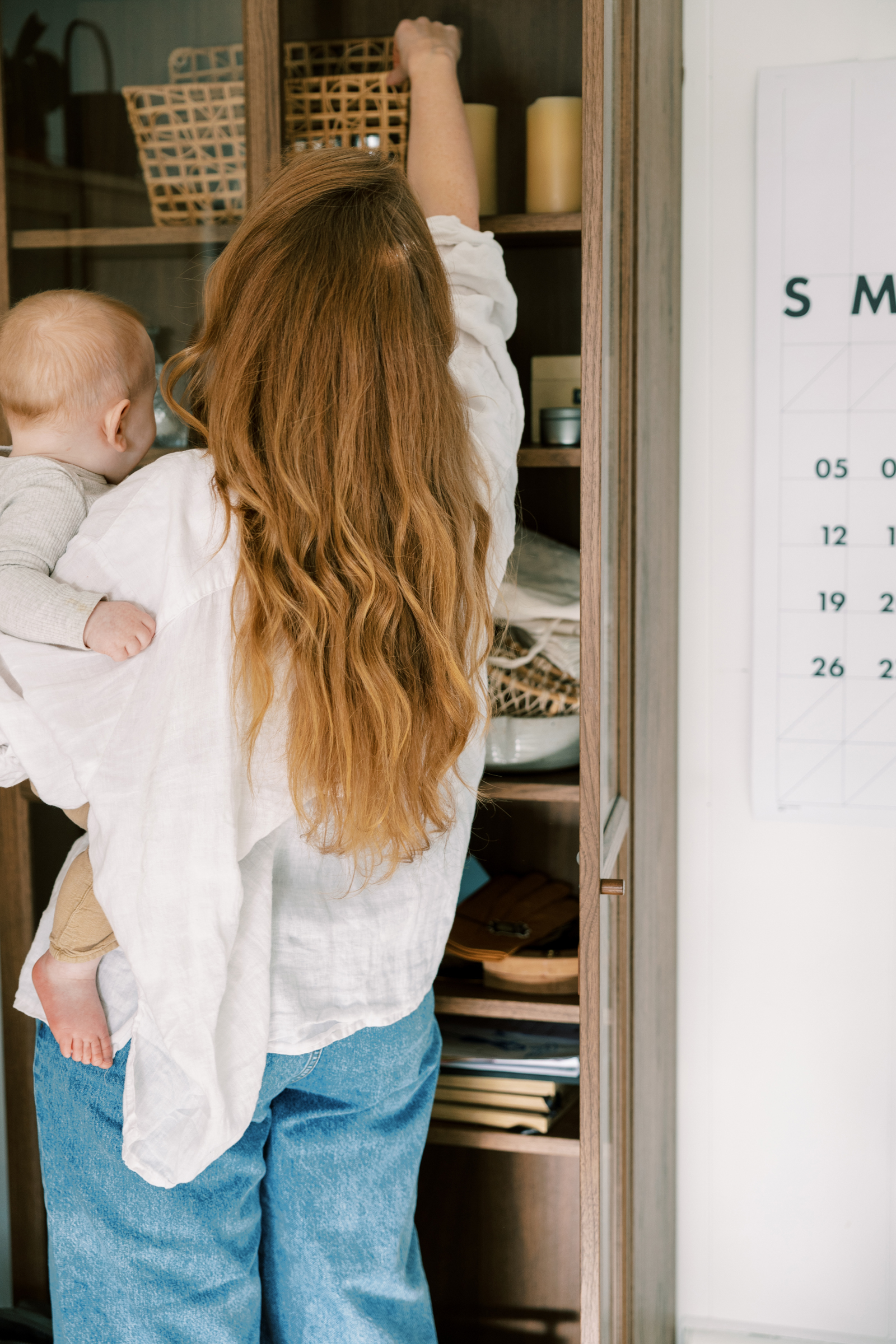 Tired new mum tidying the house while holding her baby, representing the invisible mental load and overwhelm many mothers experience during the fourth trimester.